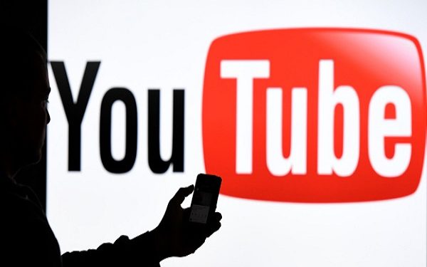 Schleswig-Holstein, Aukrug-Homfeld: A man with holds a smartphone in front of the logo of the internet platform YouTube. Photo: Carsten Rehder/dpa