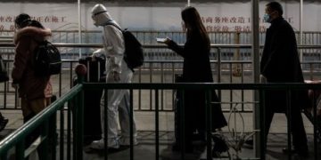 Фото: Патници, вклучително и еден кој носи заштитна опрема за целото тело, на железничката станица во Шангај овој месец/ Килаи Шен за Њујорк Тајмс
