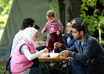 epa04928579 A migrant family from Syria, recently arrived by bus, sits at a tent village at the Donnersberg bridge close to the central train station in Munich, Germany, 13 September 2015. Munich is overwhelmed by a great number of refugees.  EPA/ANDREAS GEBERT