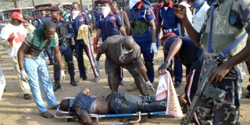 Nigerian security forces and rescuers stand around the body of a victims of an attack at Nyanya bus station in Abuja on April 14, 2014. Twin blasts at a bus station packed with morning commuters on the outskirts of Nigeria's capital killed dozens of people on April 14, in what appeared to be the latest attack by Boko Haram Islamists. The explosions rocked the Nyanya station roughly five kilometres (three miles) south of Abuja at 6:45 am (0545 GMT) and destroyed some 30 vehicles, mostly large passenger buses, officials and an AFP reporter said.  AFP PHOTO / STRINGER